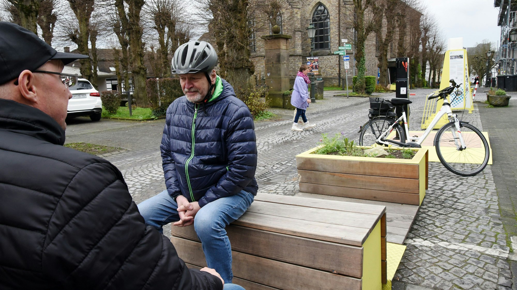 Zwei Männer sitzen auf neuen Bänken an einer Straße in Lindlar.