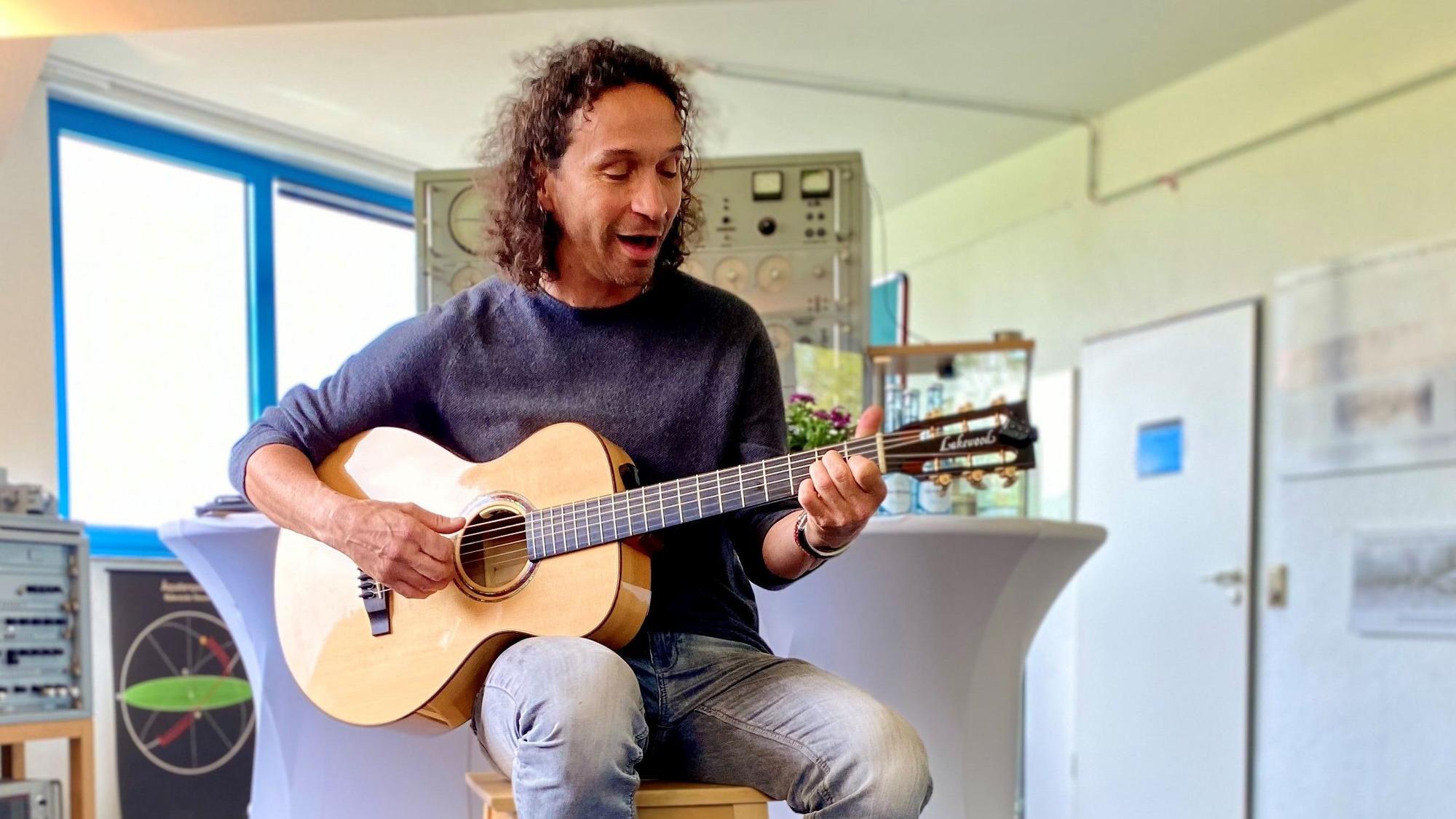 Stefan Brings sitzt mit seiner Gitarre auf einem Hocker in den Räumlichkeiten des Astropeilers Stockert und spielt ein Lied.