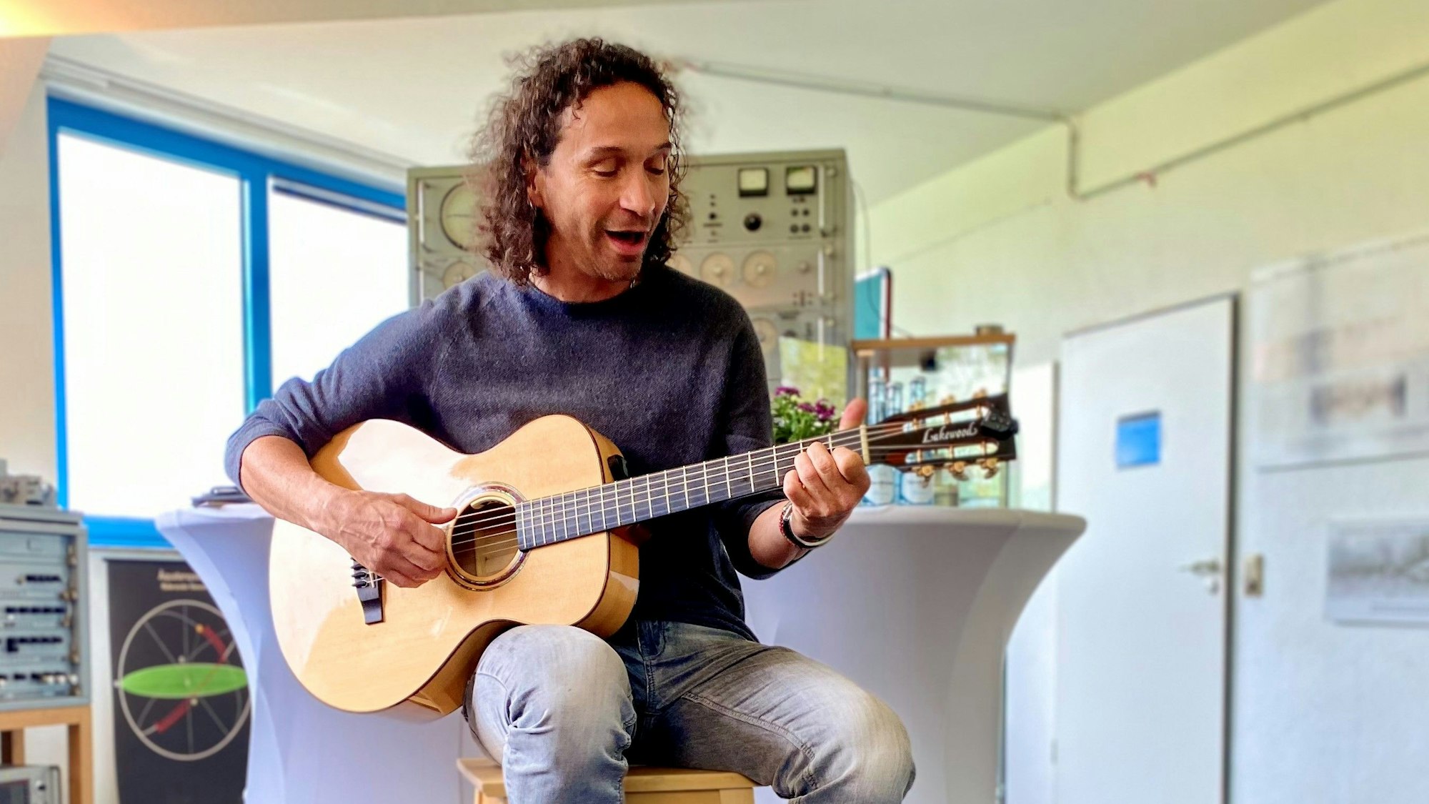 Stefan Brings sitzt mit seiner Gitarre auf einem Hocker in den Räumlichkeiten des Astropeilers Stockert und spielt ein Lied.