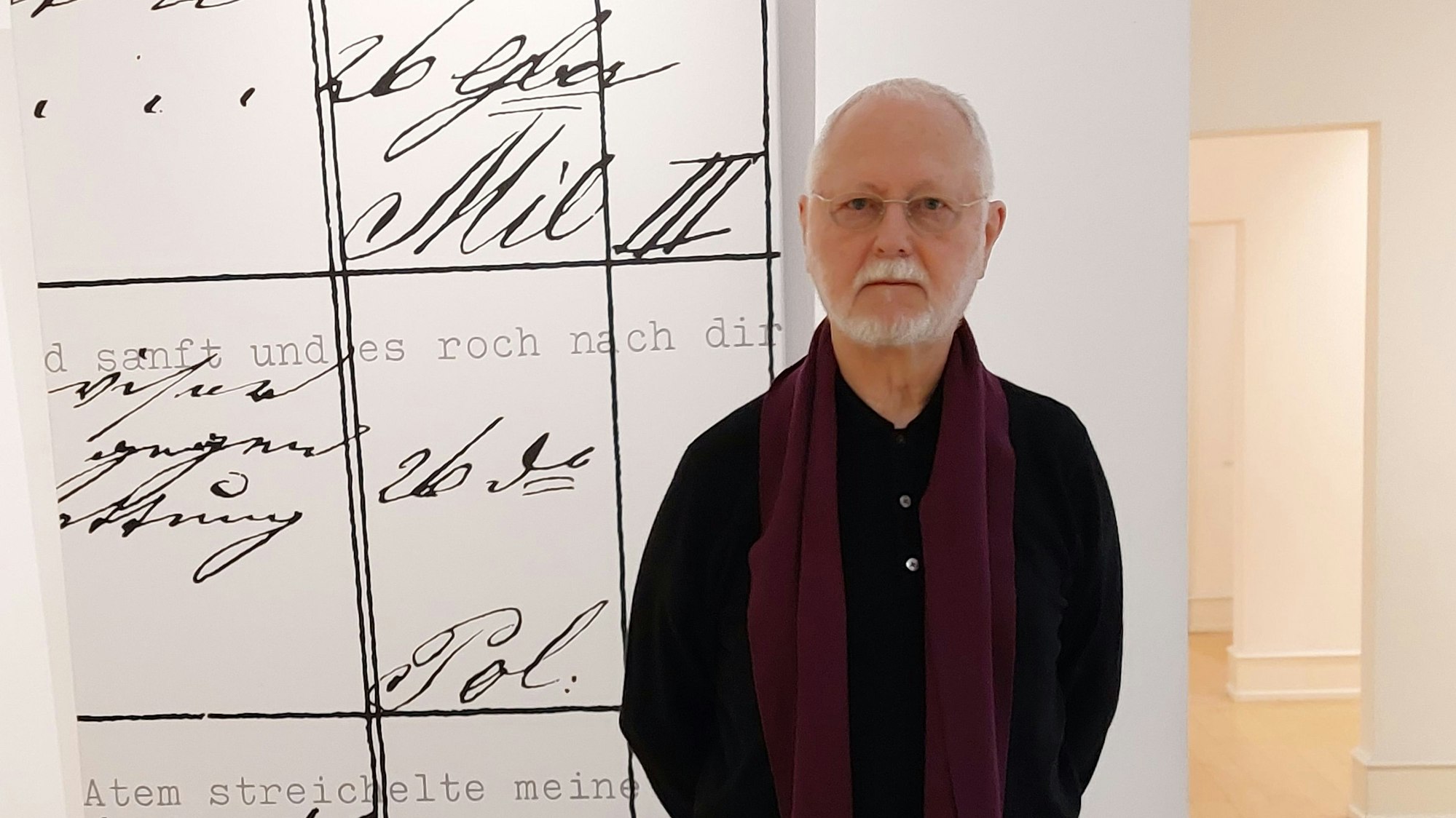 Ein älterer Herr steht vor einem großformatigen Gemälde; zu sehen sind Fragmente eines Gedichts in Schreibmaschinenschrift, außerdem Worte in einer alten Urkundenschrift.