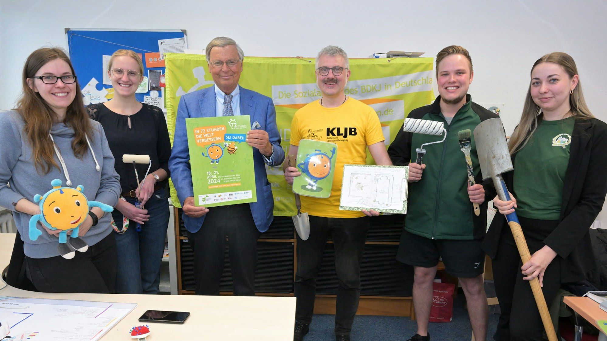 Menschen stehen mit Spaten, Plakat und anderen Utensilien beim Pressetermin zur 72-Stunden-Aktion des BDKJ in der Katholischen Jugendagentur in Bergisch Gladbach.
