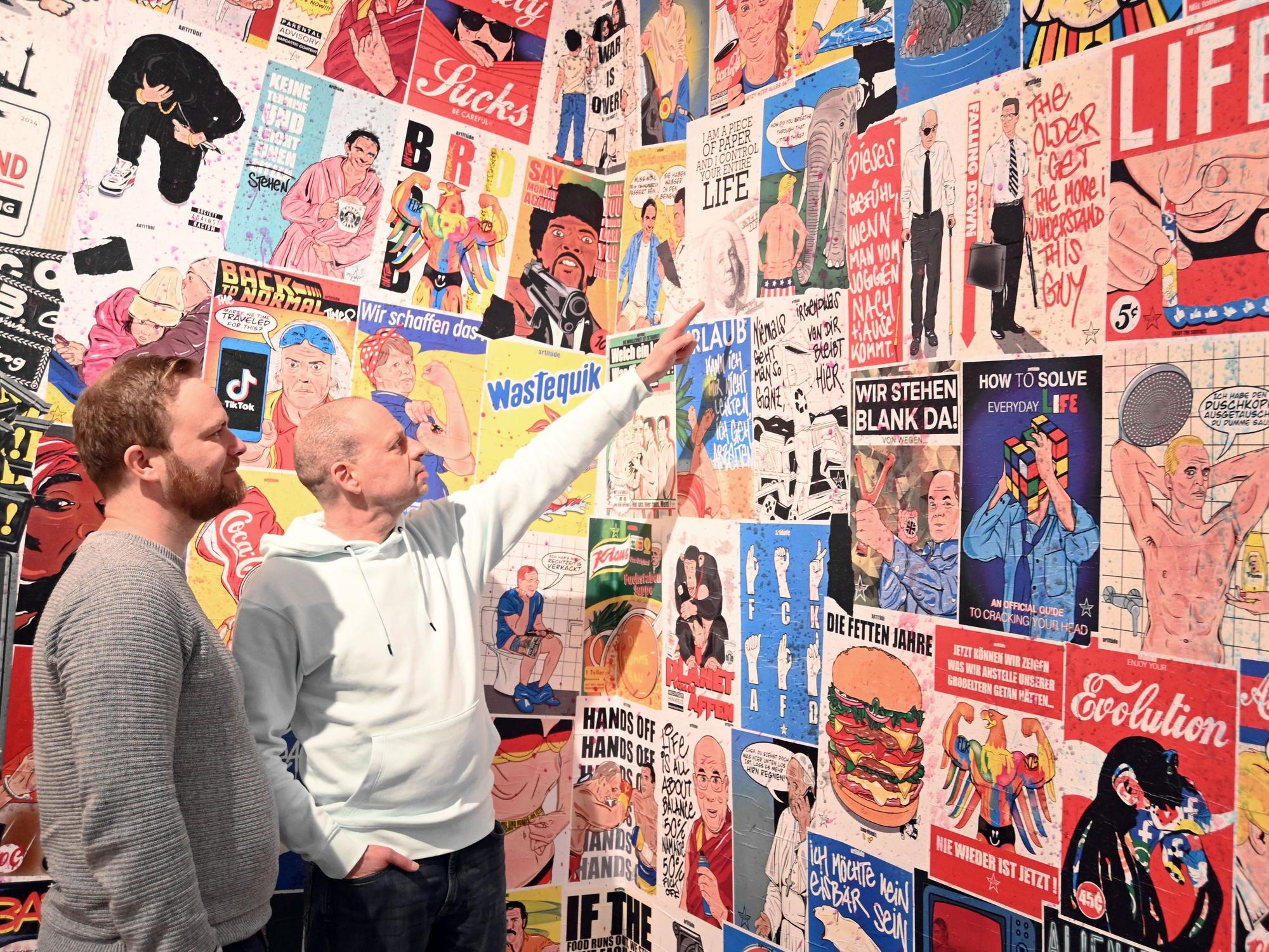Tim Ossege (l.) und Tom Weecks sind in Kölner Starßen als Künstler aktiv. Hier zeigen sie auf eine Plakatwand, die von R.F.Art gestaltet wurde.