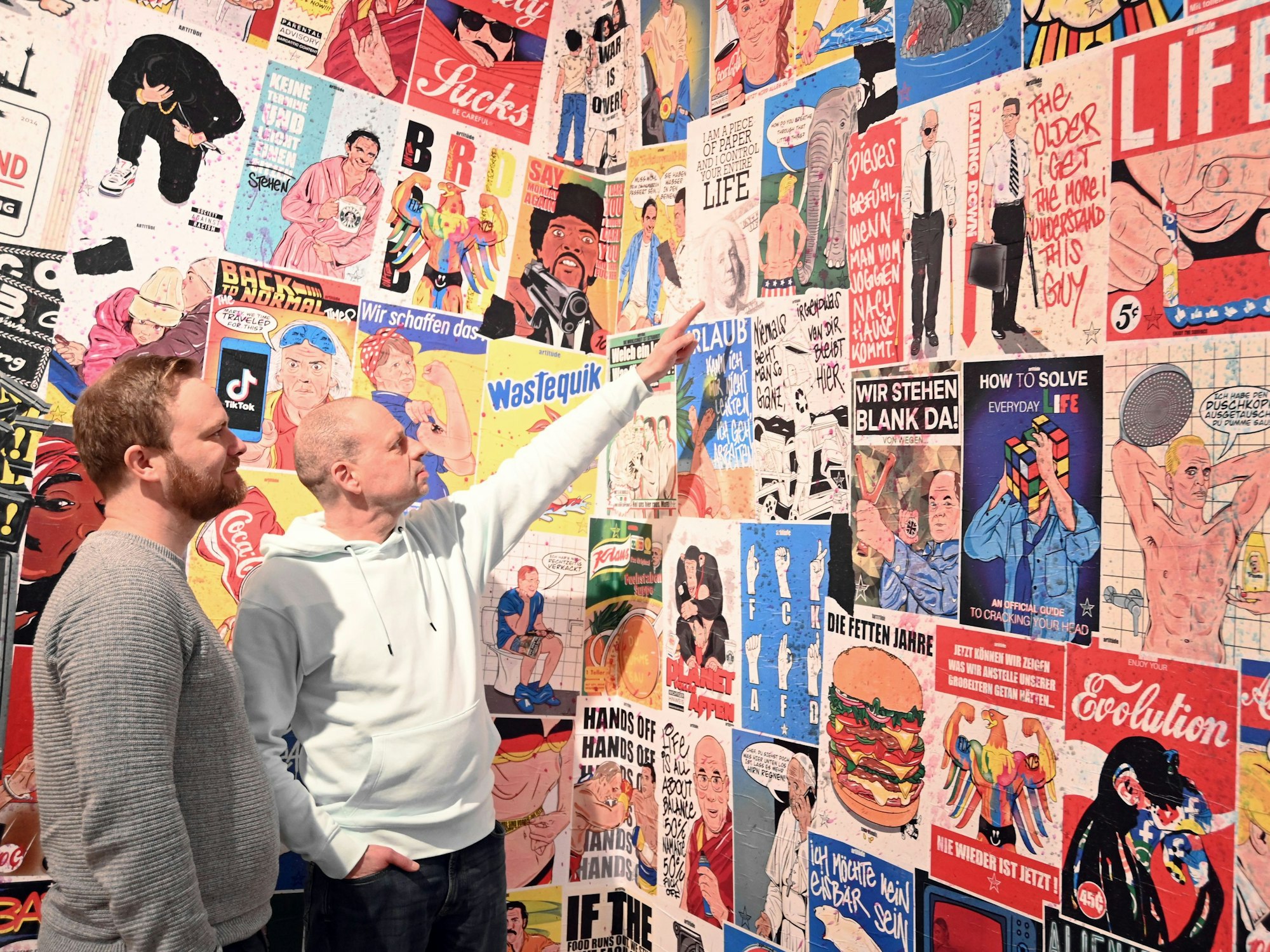 Tim Ossege (l.) und Tom Weecks sind in Kölner Starßen als Künstler aktiv. Hier zeigen sie auf eine Plakatwand, die von R.F.Art gestaltet wurde.