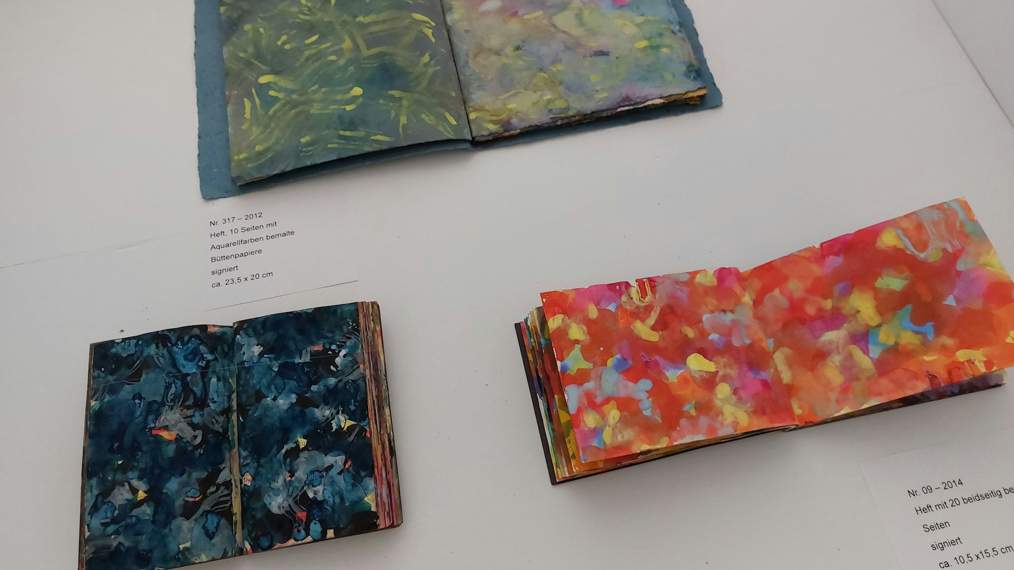 Drei Hefte in einem kleinen Format; die Seiten sind sehr bunt und abstrakt gestaltet. Eines der Bücher ist als Gebetbuch ausgewiesen