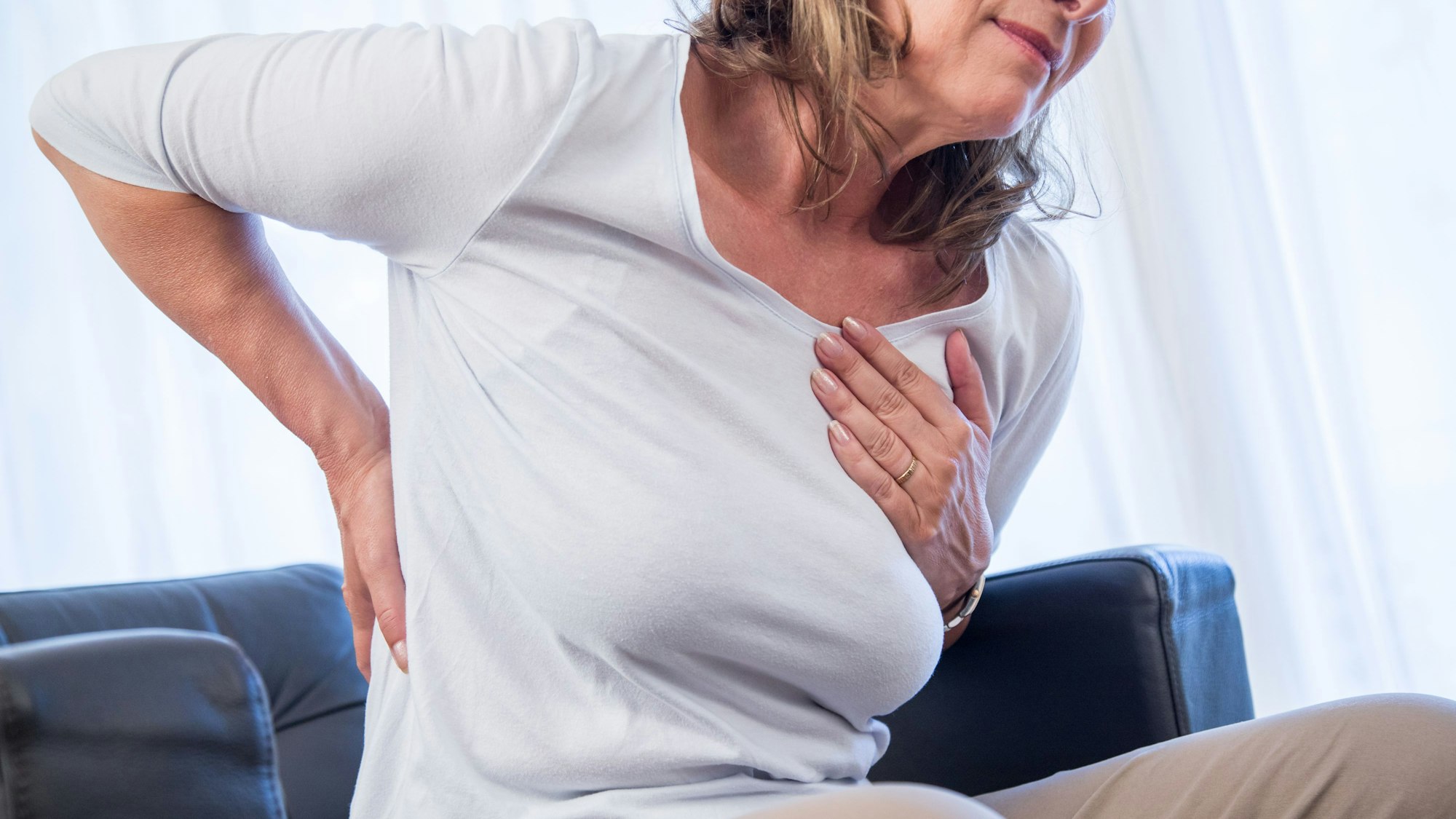 Eine Frau hält sich die Hände an Brustkorb und Rücken, als hätte sie Schmerzen