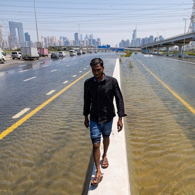 Ein Mann läuft über eine Mauer zwischen zwei überfluteten Straßen in Dubai. Experten halten Cloud Seeding nicht für den Grund für die heftigen Regenfälle in den Vereinigten Arabischen Emiraten.
