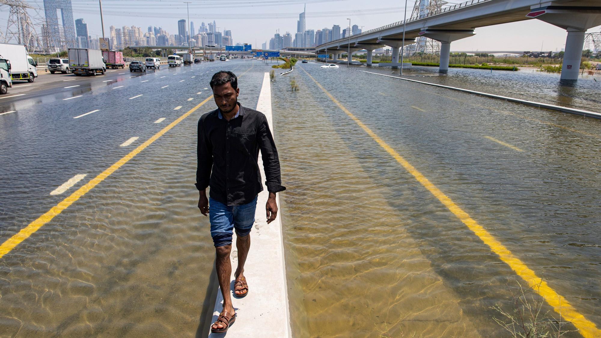 Ein Mann läuft über eine Mauer zwischen zwei überfluteten Straßen in Dubai. Experten halten Cloud Seeding nicht für den Grund für die heftigen Regenfälle in den Vereinigten Arabischen Emiraten.