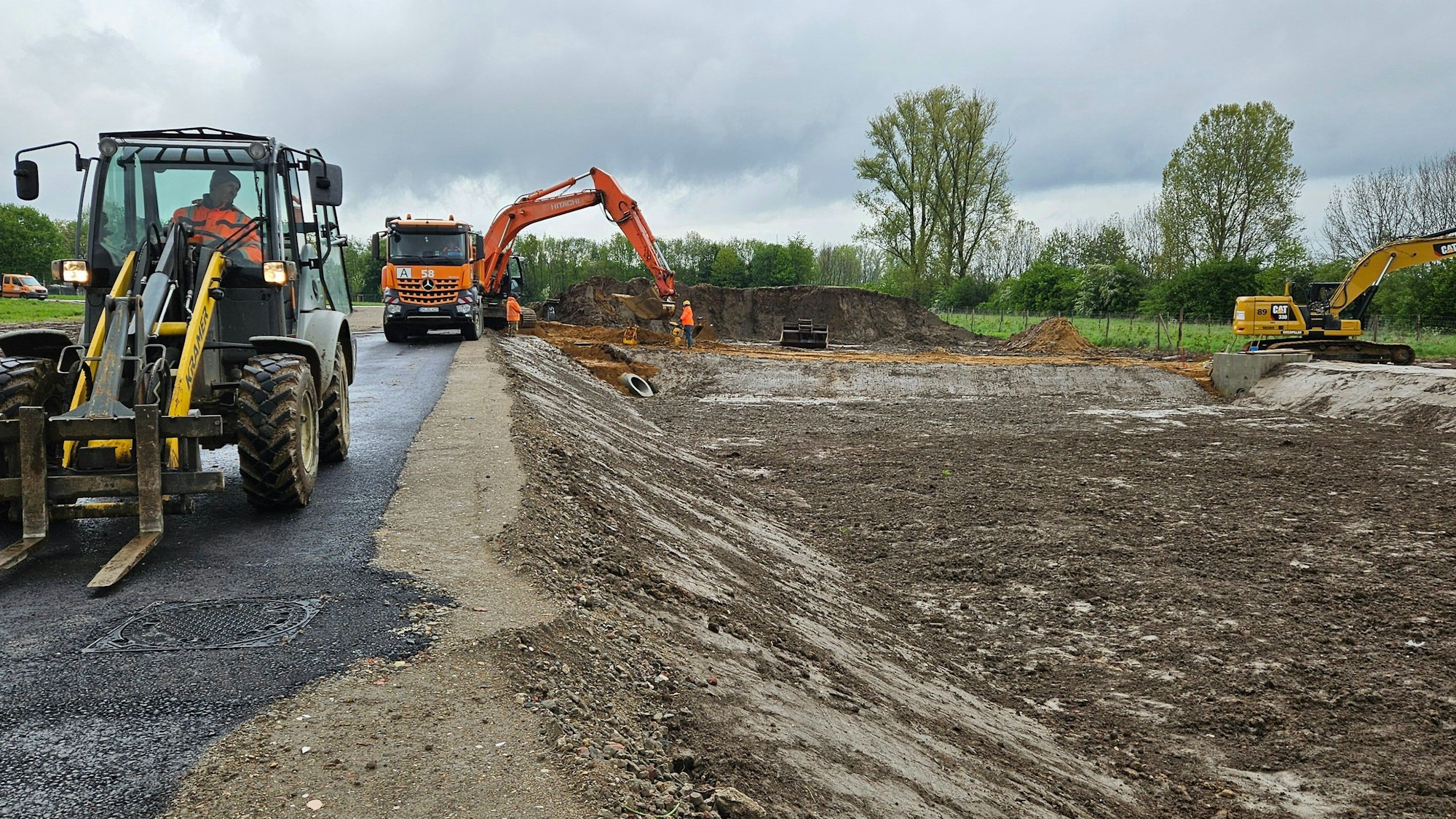 Bagger und andere Baufahrzeuge stehen an einem unbebauten Grundstück.