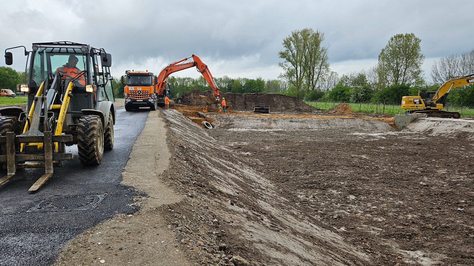Bagger und andere Baufahrzeuge stehen an einem unbebauten Grundstück.