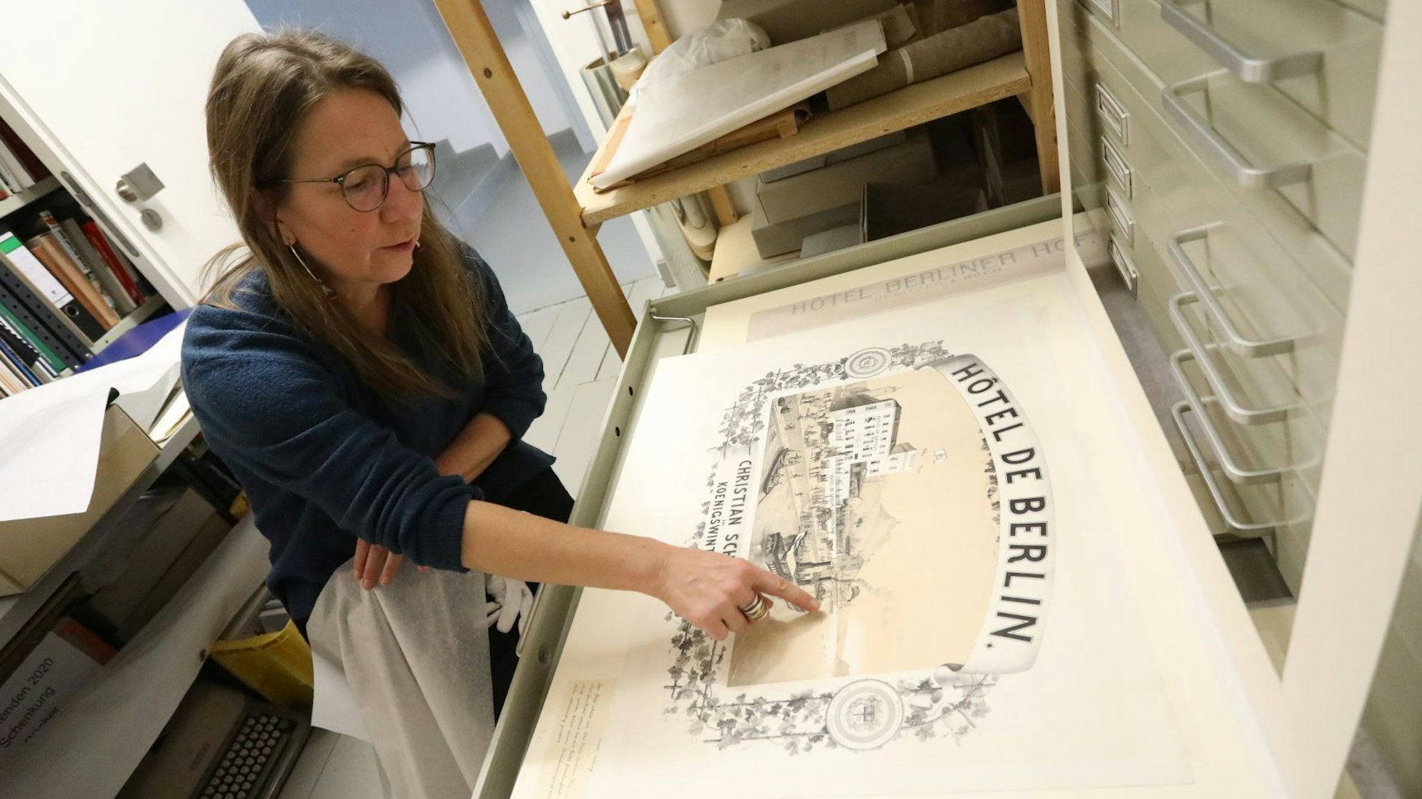 Eine Frau zeigt auf ein historisches Plakat aus dem 19. Jahrhundert.