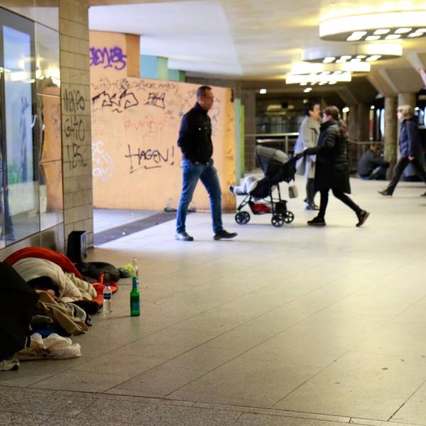 Obdachlose liegen tagsüber am Wiener Platz, im Hintergrund gehen Passanten an ihnen vorbei.