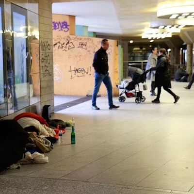Obdachlose liegen tagsüber am Wiener Platz, im Hintergrund gehen Passanten an ihnen vorbei.