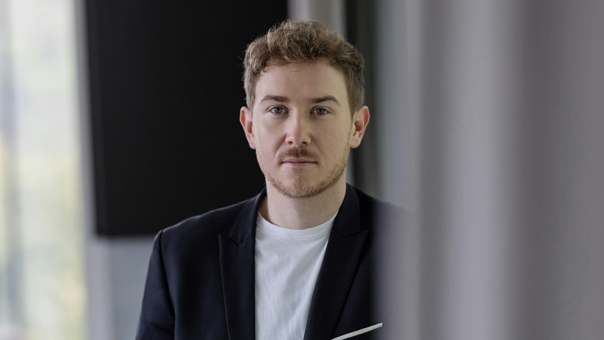 Der 30-jährige Zukunftsforscher Tristan Horx trägt ein weißes T-Shirt unter dem blauen Anzug und einen kurzen Bart.