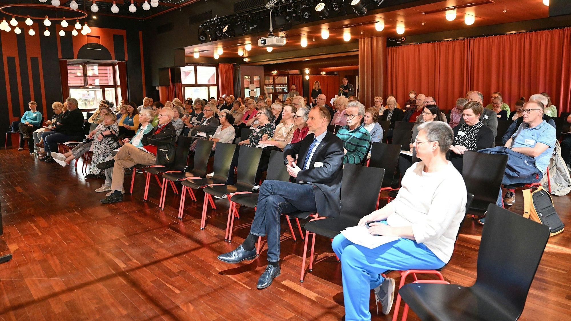 Auf Stühlen sitzen in dem Saal die Teilnehmer.