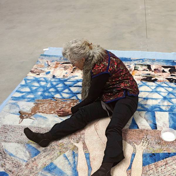 Kiki Smith sitzt auf einer über den Boden ausgebreiteten Papiercollage und malt mit einem Stift.