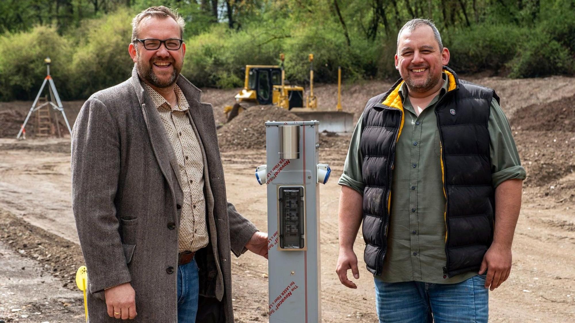 Thomas Hambach (l.) und Christian Klein stehen auf der Baustelle des neuen Wohnmobilhafens bei Mechernich. Im Hintergrund ist eine Planierraupe zu sehen.