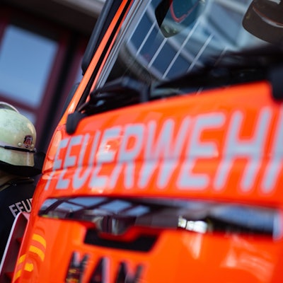 Eine Einsatzkraft der Feuerwehr steht neben einem Einsatzfahrzeug der Feuerwehr.