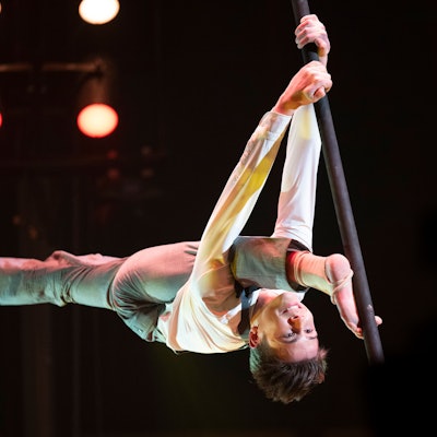 Justin Philadelphia hängt im Spagat kopfüber an einer Stange.