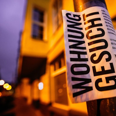 Ein Zettel mit der Aufschrift „Wohnung gesucht“ hängt vor Wohnhäusern.