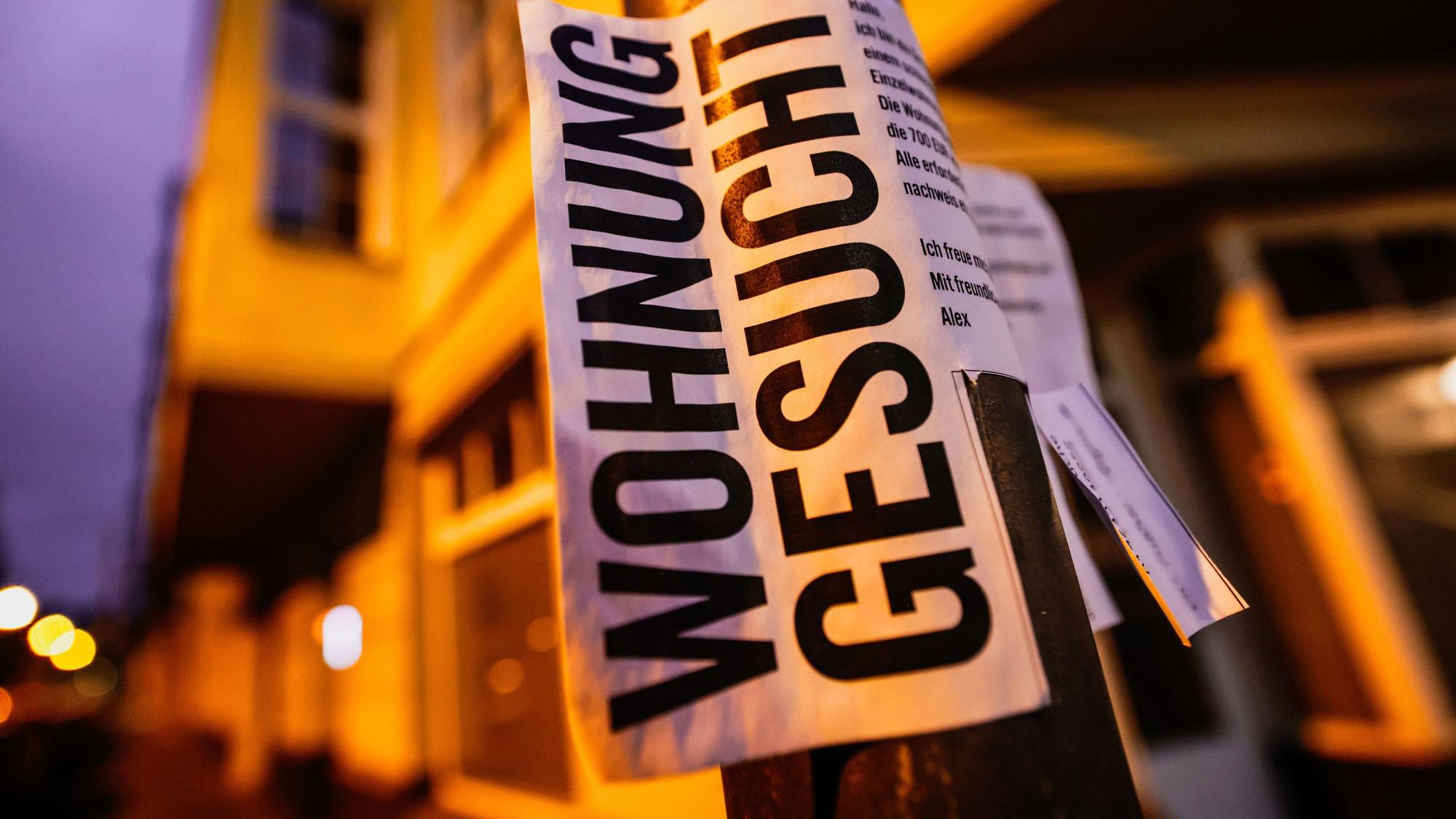 Ein Zettel mit der Aufschrift „Wohnung gesucht“ hängt vor Wohnhäusern.