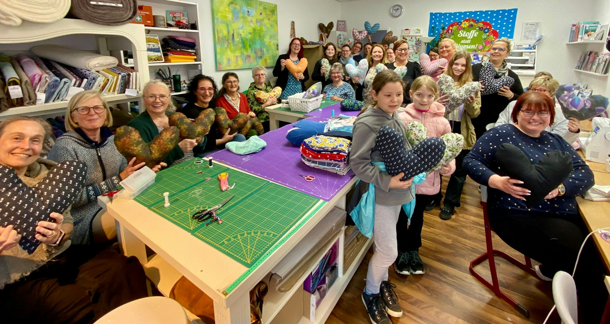 Auf dem Foto sind Frauen und Kinder mit Herzkissen in einem Nähraum zu sehen.