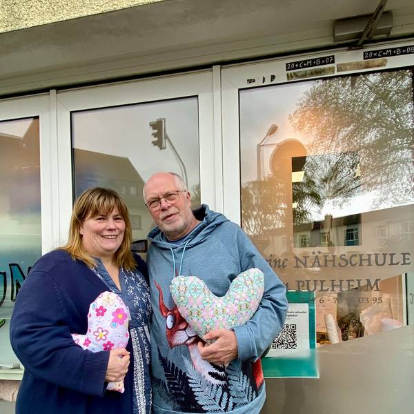 Auf dem Foto sind Heike Baier-Lücke und Thomas Lücke zu sehen. Sie haben den Kölner Herzkissen Verein gegründet, um mit Herzkissen Brustkrebspatientinnen zu unterstützen. Sie halten Herzkissen in der Hand.