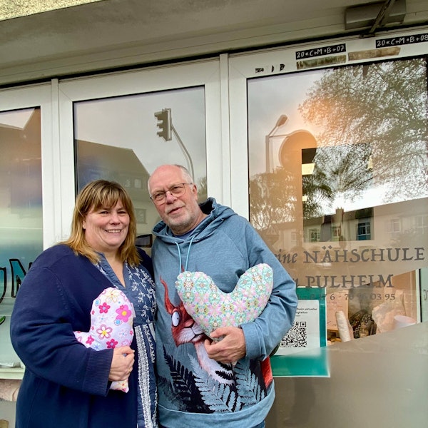 Auf dem Foto sind Heike Baier-Lücke und Thomas Lücke zu sehen. Sie haben den Kölner Herzkissen Verein gegründet, um mit Herzkissen Brustkrebspatientinnen zu unterstützen. Sie halten Herzkissen in der Hand.