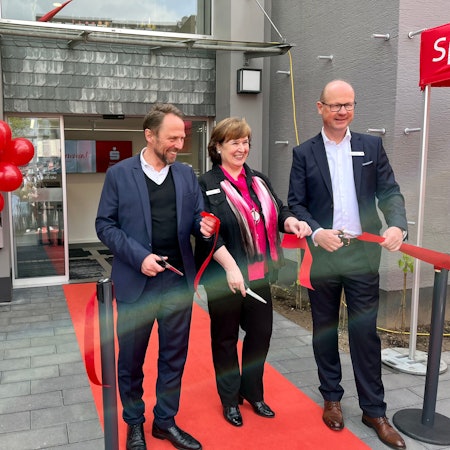 OB Uwe Richrath, Filialleiterin Heike Schulz und Sparkassenvorstand Markus Grawe schneiden vor der umgebauten Filiale in Lützenkirchen ein rotes Band durch.