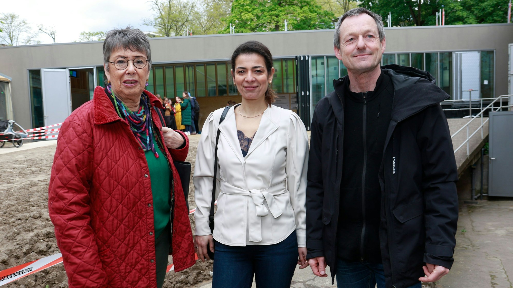 Zu sehen sind zwei Frauen und ein Mann, die vor einem Gebäude auf einer Baustelle stehen.
