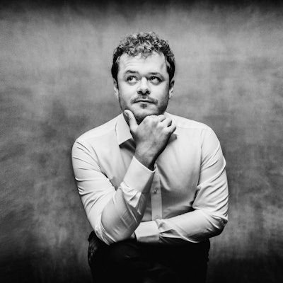 Das schwarz-weiße Bild zeigt Benjamin Grosvenor in nachdenklicher Pose, das Kinn stützt er mit der Hand. Der Hintergrund wirkt rauchig-verworren.