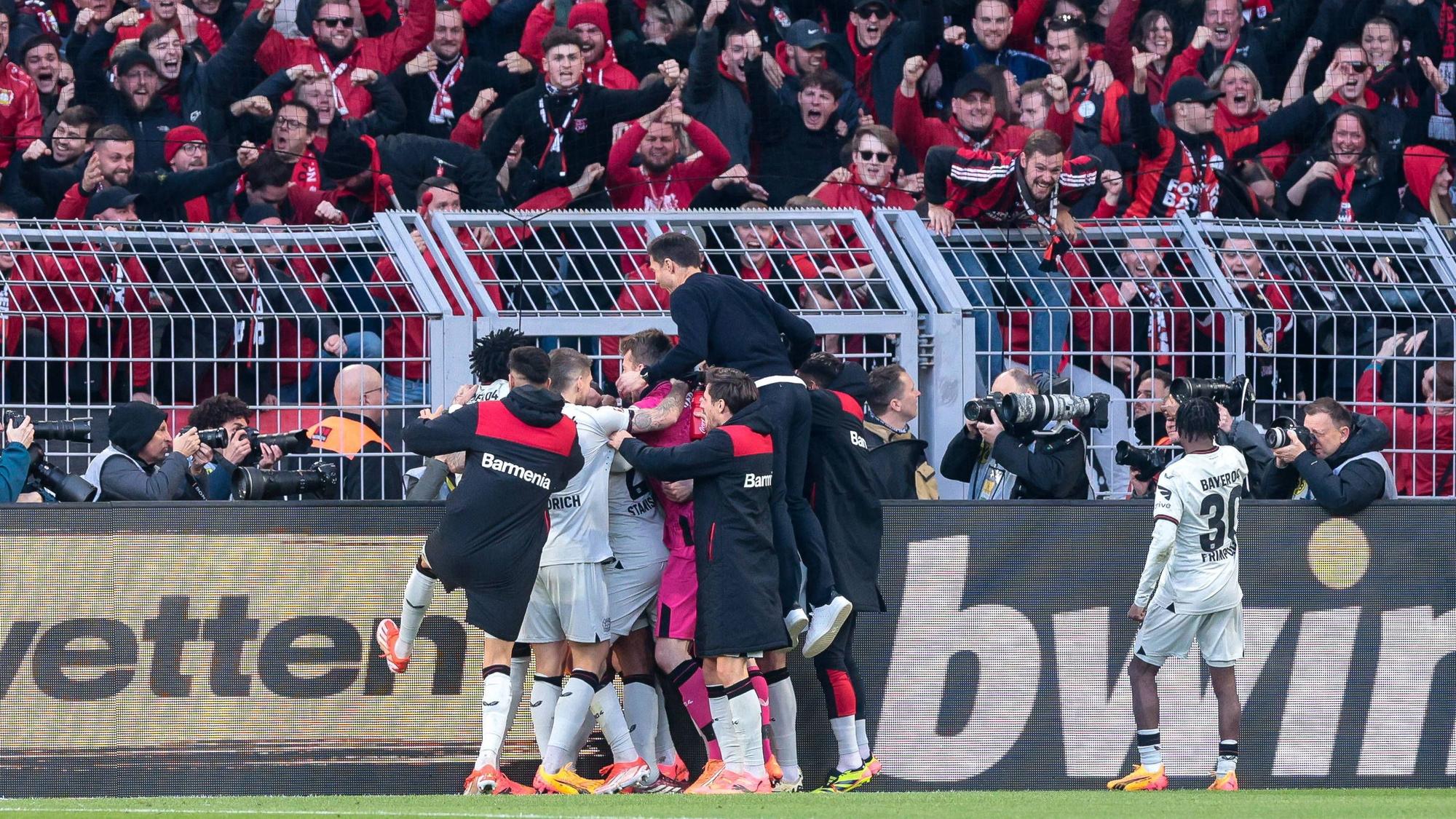 Die Leverkusener bejubeln vor den angereisten Fans den späten Ausgleichstreffer durch Josip Stanisic. Trainer Alonso wirft sich auf die Jubeltraube.