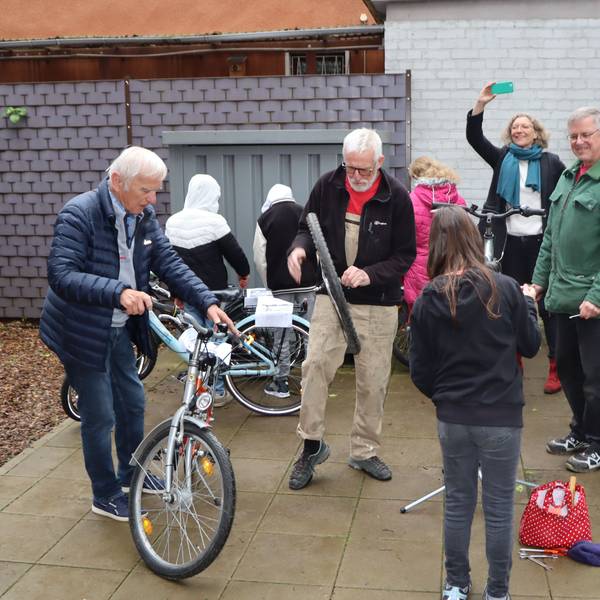 Ehrenamtler vom Repair-Café reparieren zwei Fahrräder. Schülerinnen und Schüler helfen dabei mit.