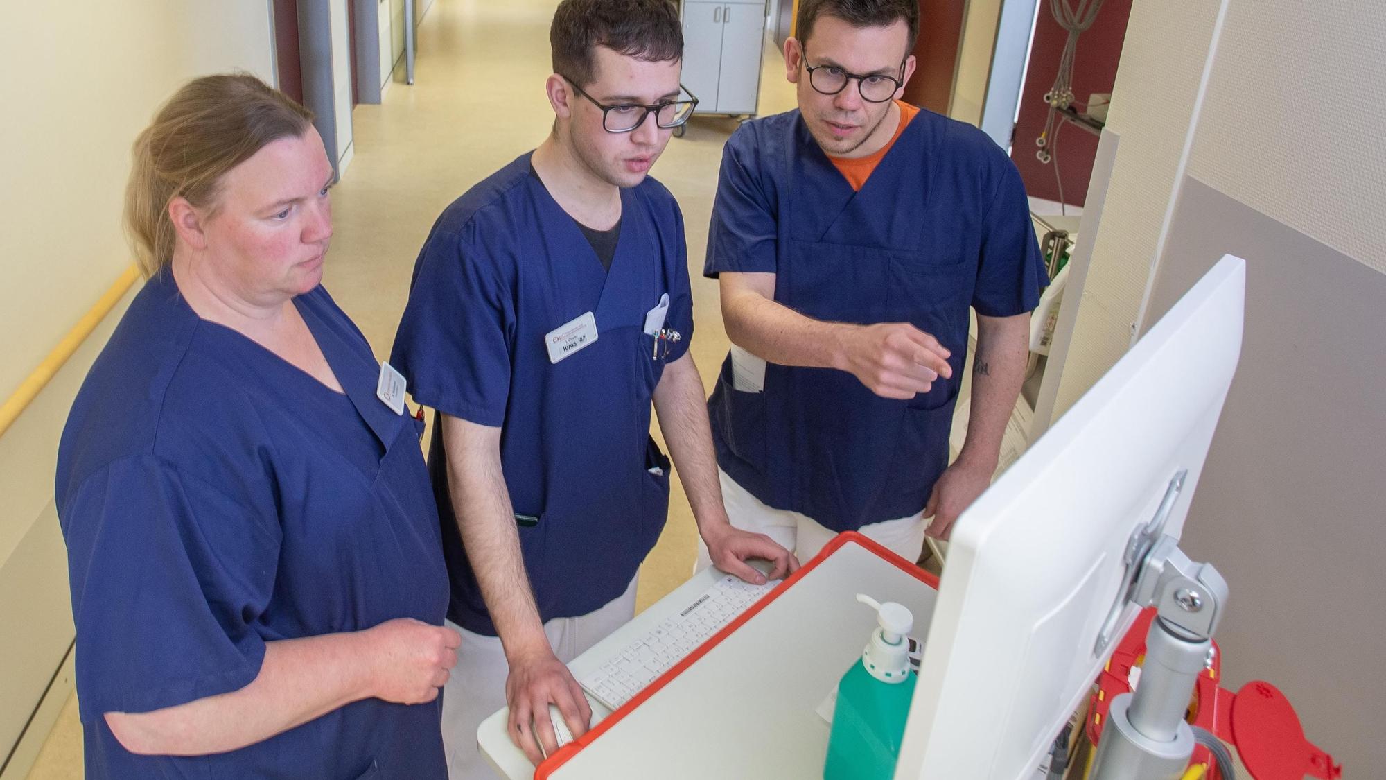 Besprechung: Projektleiter Jonas Sebastian Schütter Gesundheits- und Bildungszentrum des Klinikums Oberberg (rechts) mit Schüler Ilyas Chaibi aus Marienheide und Praxisanleiterin Nicole Wurzbacher. Die Gruppe steht an einem Computer auf dem Klinikflur.
