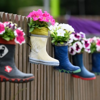 Kinder-Gummistiefel mit Blumen hängen an einem Zaun einer Kindertagesstätte.