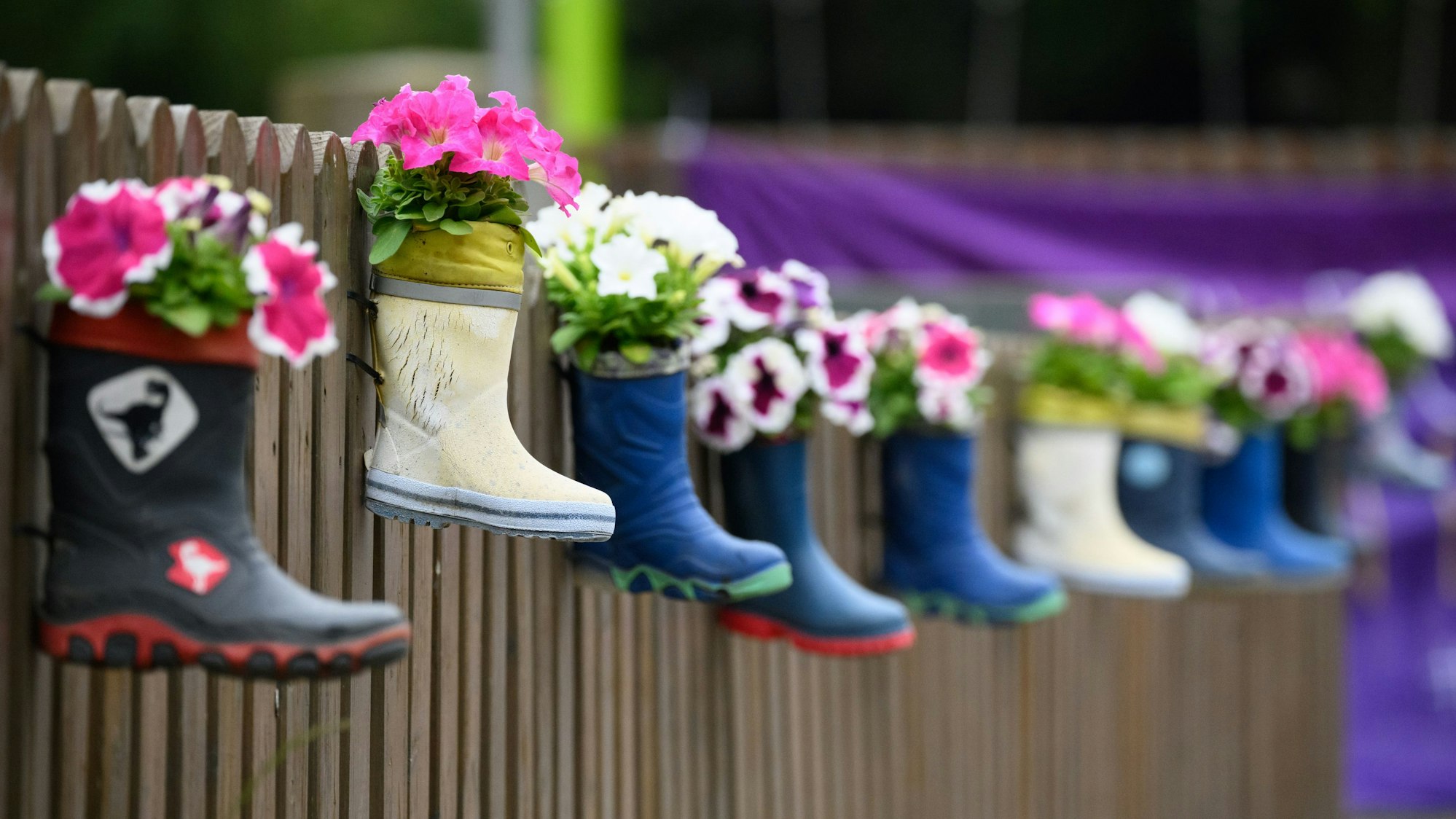 Kinder-Gummistiefel mit Blumen hängen an einem Zaun einer Kindertagesstätte.