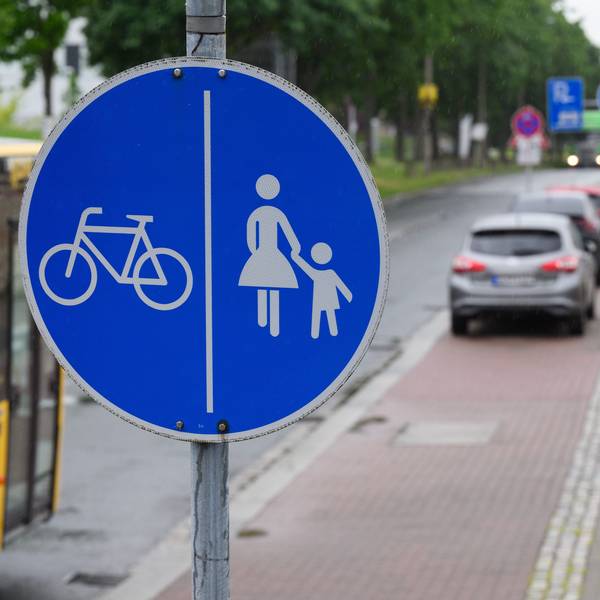 Ein Schild für einen getrennten Rad- und Gehweg steht vor dem Ende eines Radweges und dem Beginn der Zone, in der das Parken auf dem halben Gehweg erlaubt ist.