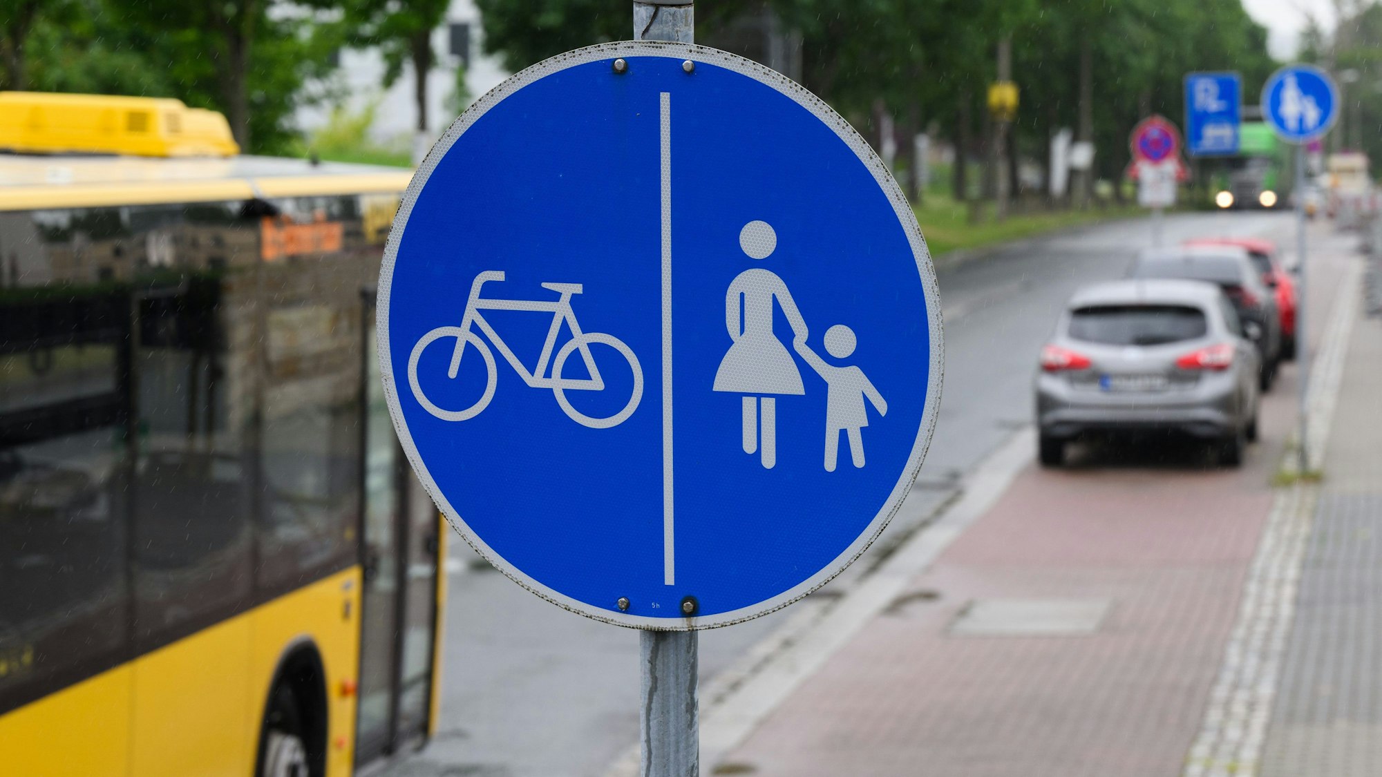 Ein Schild für einen getrennten Rad- und Gehweg steht vor dem Ende eines Radweges und dem Beginn der Zone, in der das Parken auf dem halben Gehweg erlaubt ist.