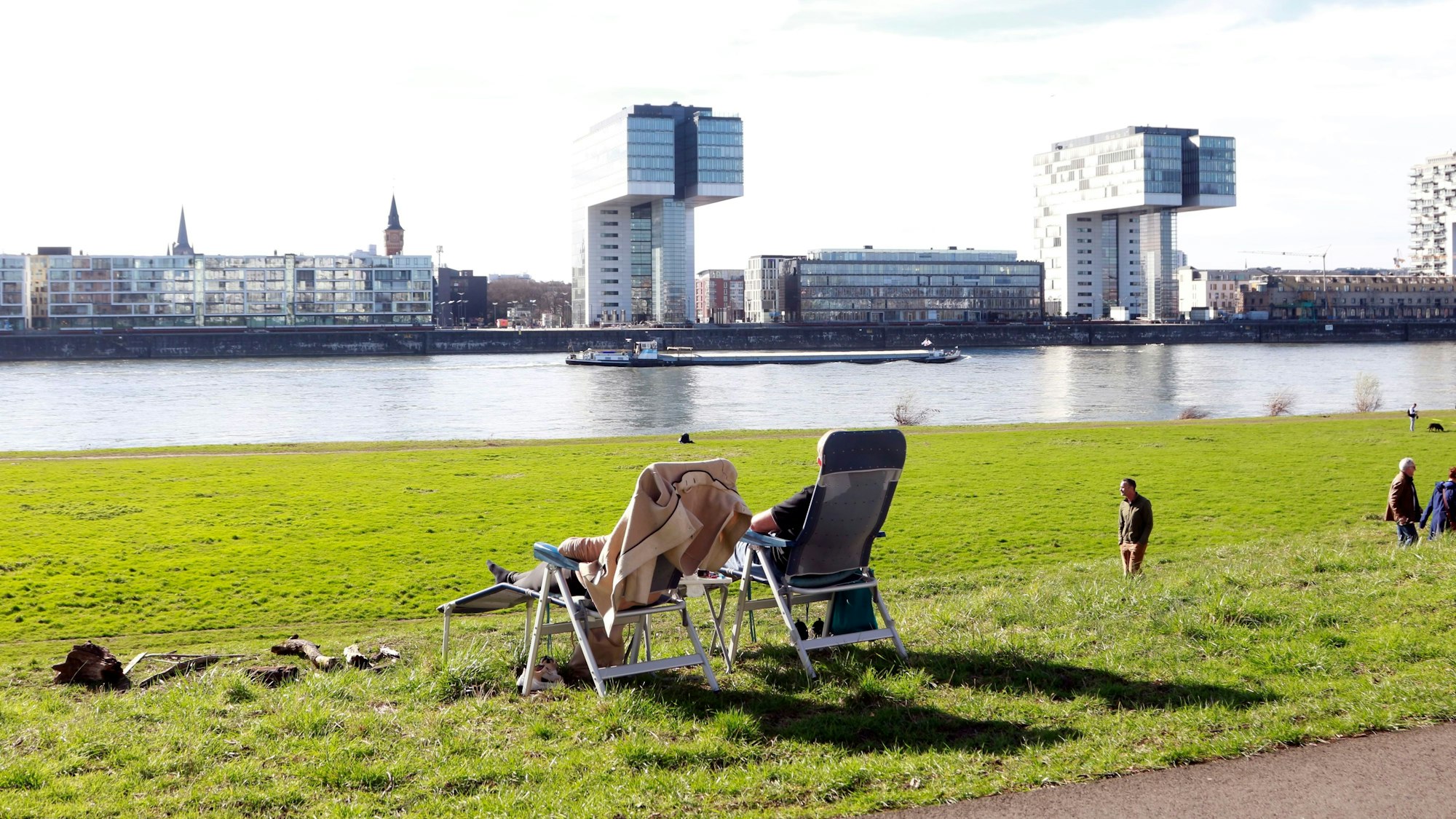 An der Alfred-Schütte-Allee, mit Panorama auf die Kölner Kranhäuser, liegen zwei auf ihren Sonnenliegen und genießen den Ausblick.