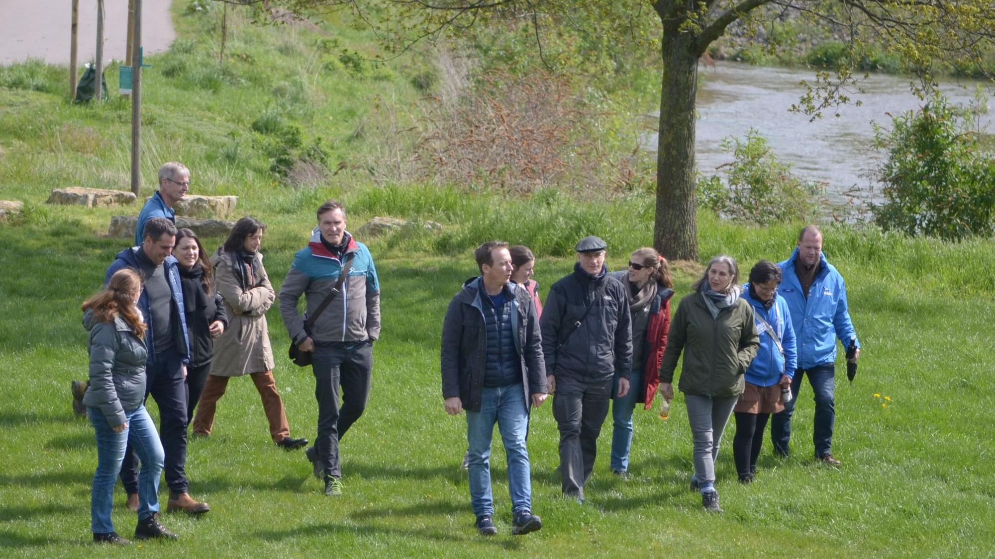 Eine Gruppe von Männern und Frauen geht über eine Wiese, im Hintergrund die Erft.