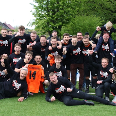Spieler der SG Keldenich-Scheven jubeln. Zwei halten das Trikot mit der Nr. 14 in die Höhe.