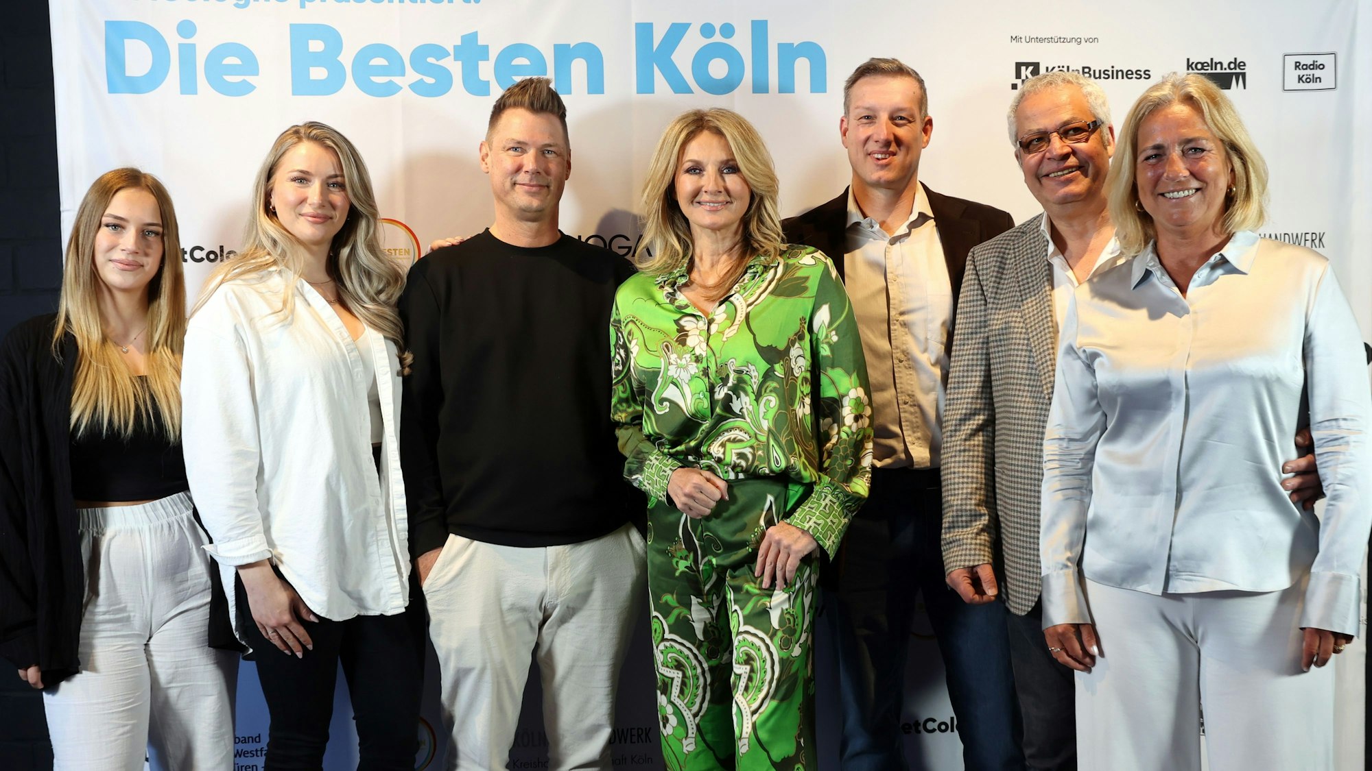 Sieben Menschen stehen vor einer Plakatwand mit der Aufschrift„ Die Besten Köln“. V.l.n.r.: Mia und Sophie Péus mit dem Vater Norbert Schulze, Frauke Ludovig, Dr. Mario Binder und Raimundo und Kerstin Aparicio.