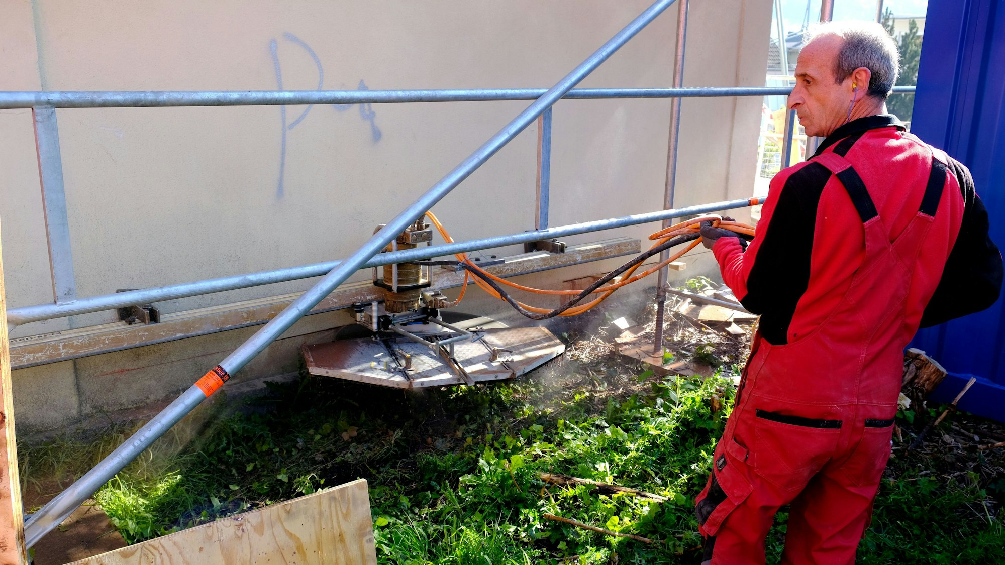 Ein Bauarbeiter in roter Arbeitskleidung setzt mit einer Steinsäge einen Schnitt an der massiv gemauerten Stirnseite des Wartesaals.
