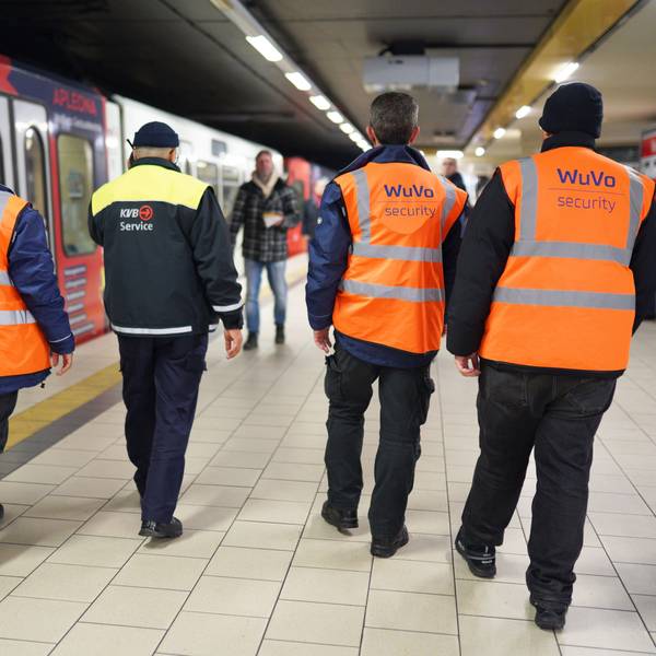 Zu sehen sind vier Männer an einer KVB-Haltestelle in der Rückansicht.
