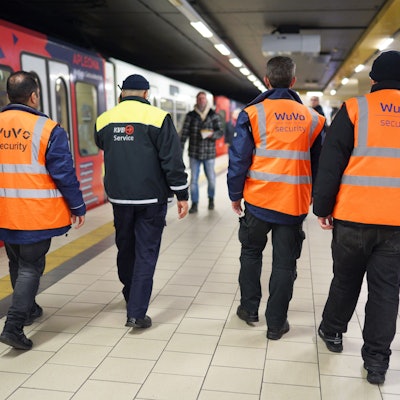 Zu sehen sind vier Männer an einer KVB-Haltestelle in der Rückansicht.