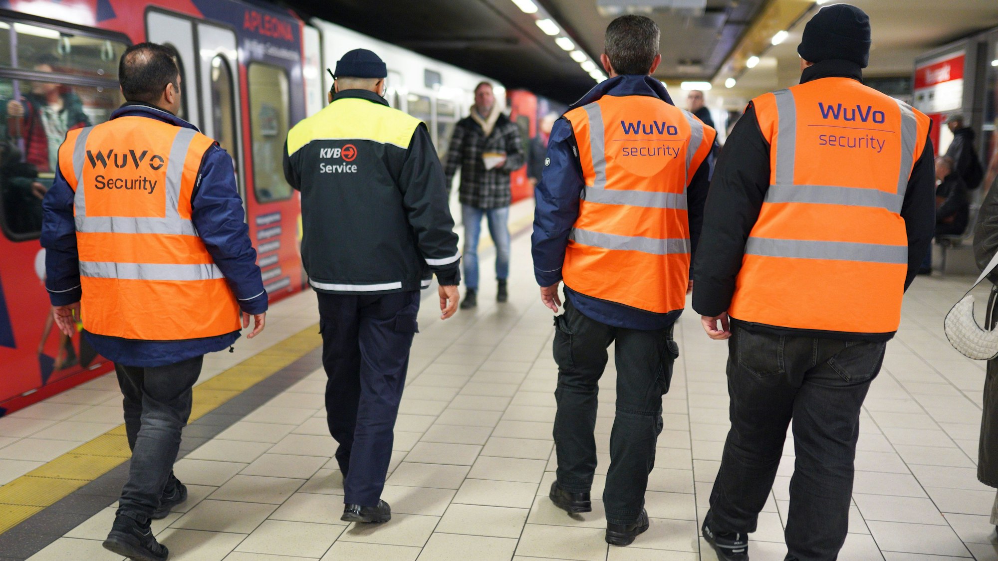 Zu sehen sind vier Männer an einer KVB-Haltestelle in der Rückansicht.