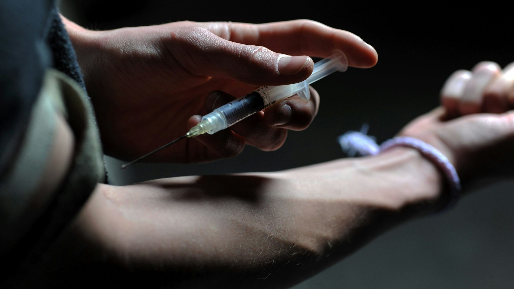 Ein Mann hält eine Heroinspritze an seinen Arm. (Illustration)