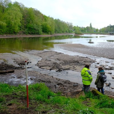 Der Kommerner Mühlensees hat kaum noch Wasser, viele Stellen treten inselartig hervor. Zwei Personen stehen am Rand.