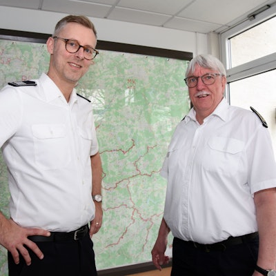 Der neue Kreisbrandmeister und scheidende Kreisbrandmeister Wilfried Fischer des Oberbergischen Kreises stehen vor einer Kreiskarte nebeneinander.