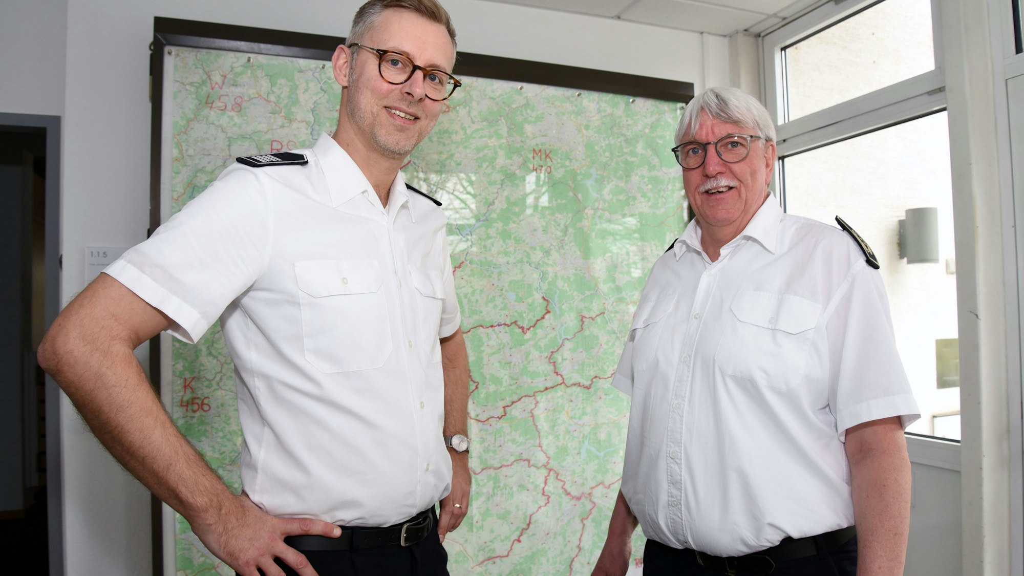 Der neue Kreisbrandmeister und scheidende Kreisbrandmeister Wilfried Fischer des Oberbergischen Kreises stehen vor einer Kreiskarte nebeneinander.