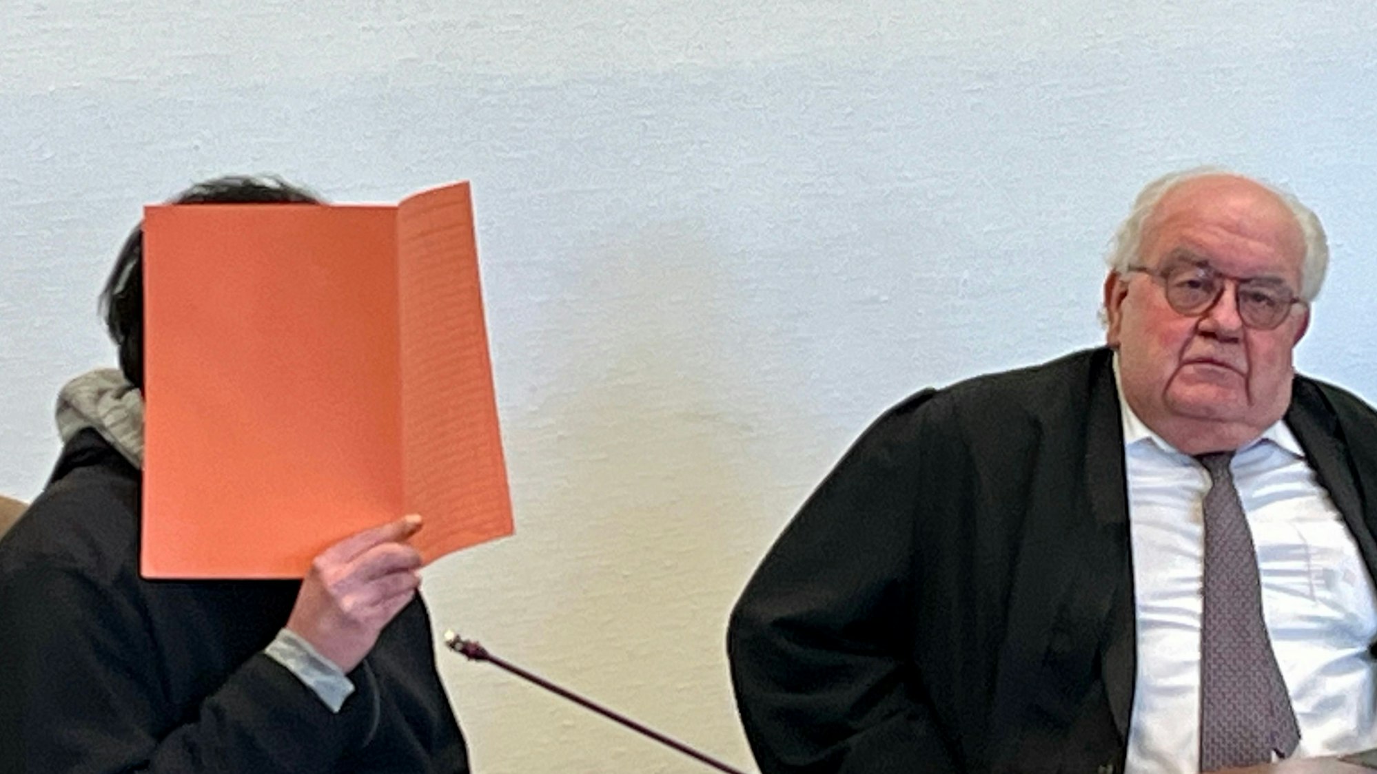 Der Mann, der am 27. Oktober 2023 seine Freundin in Rheindorf auf offener Straße getötet haben soll, sitzt, verborgen hinter einer Aktenmappe, neben seinem Anwalt Gottfried Reims im Kölner Landgericht.